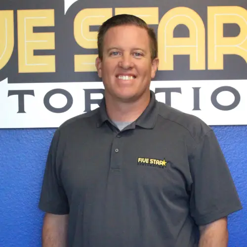 A person in a dark gray polo shirt stands in front of a large "Five Star" sign against a blue wall.